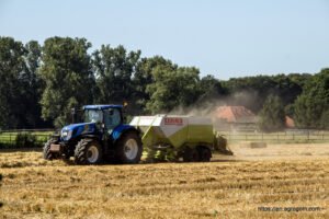 A tractor towing a baler makes hay bales in a field in Germany